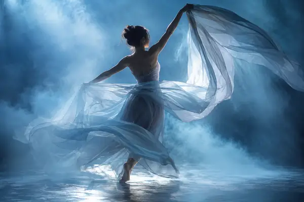 A dancer holding translucent fabric in a soft blue mist-filled studio.